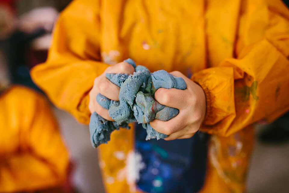 
            
                Ein Kind in gelbem Kittel hält Knetmasse in den Händen
            
        