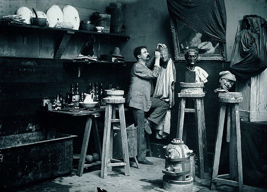 Black and white photograph of the artist Medardo Rosso in his studio surrounded by his works, 1906