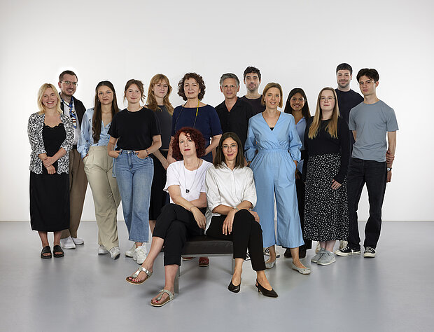 
            
                a group of people in front of a white wall, four of them sitting on a bench in the foreground: the marketing and communication team at mumok
            
        