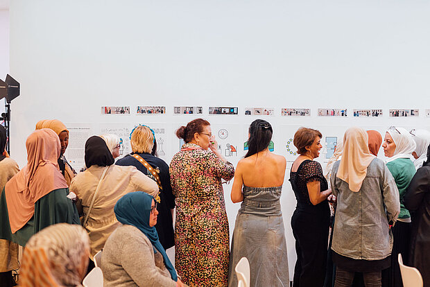 
            
                mehrere Frauen stehen vor einer weißen Wand, auf der kleine Bilder angebracht sind - sie scheinen sie anzusehen und darüber zu sprechen
            
        
