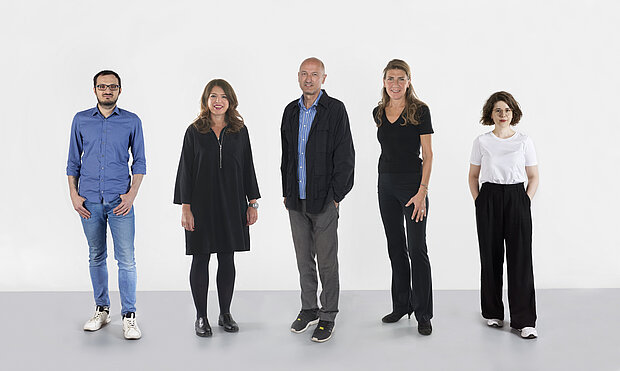 
            
                four standing people in front of a white wall
            
        