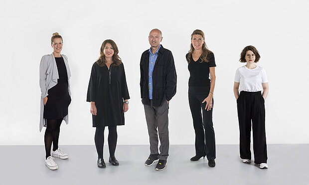 
            
                four standing people in front of a white wall
            
        